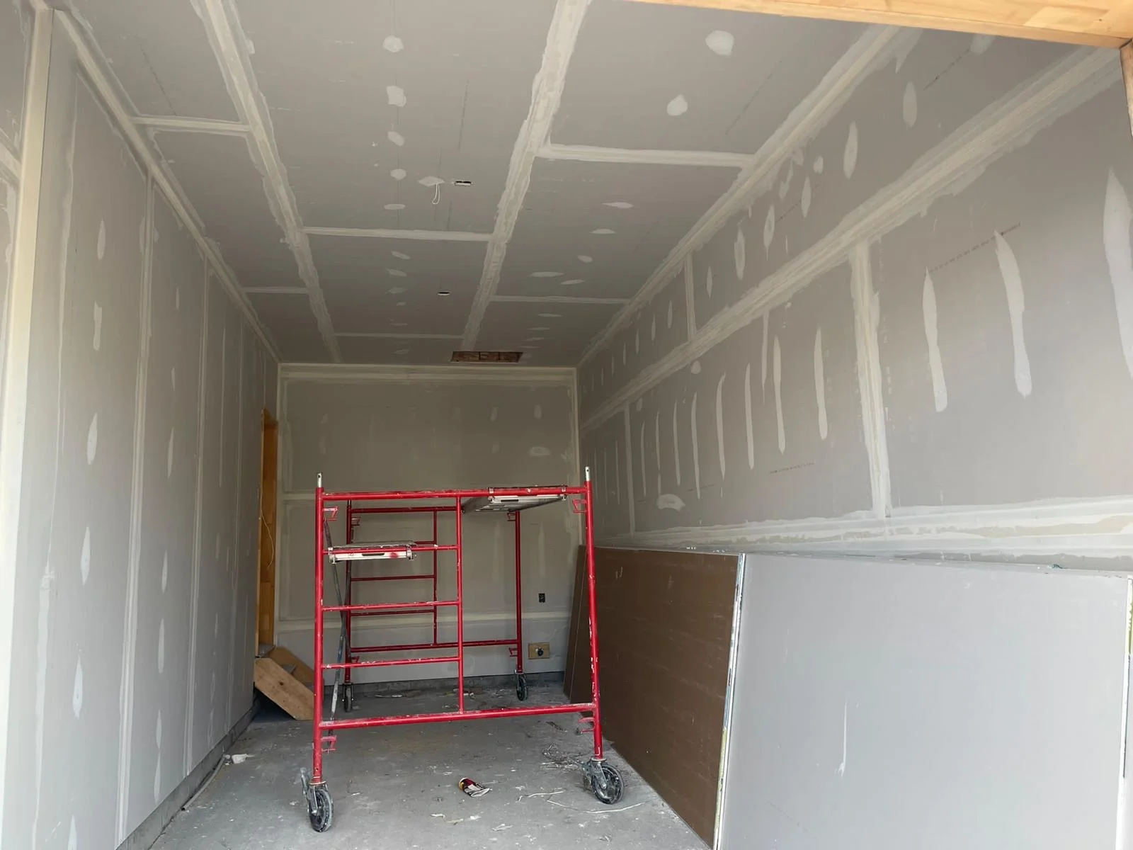 Room with taped drywall seams and a rolling scaffold for ceiling access