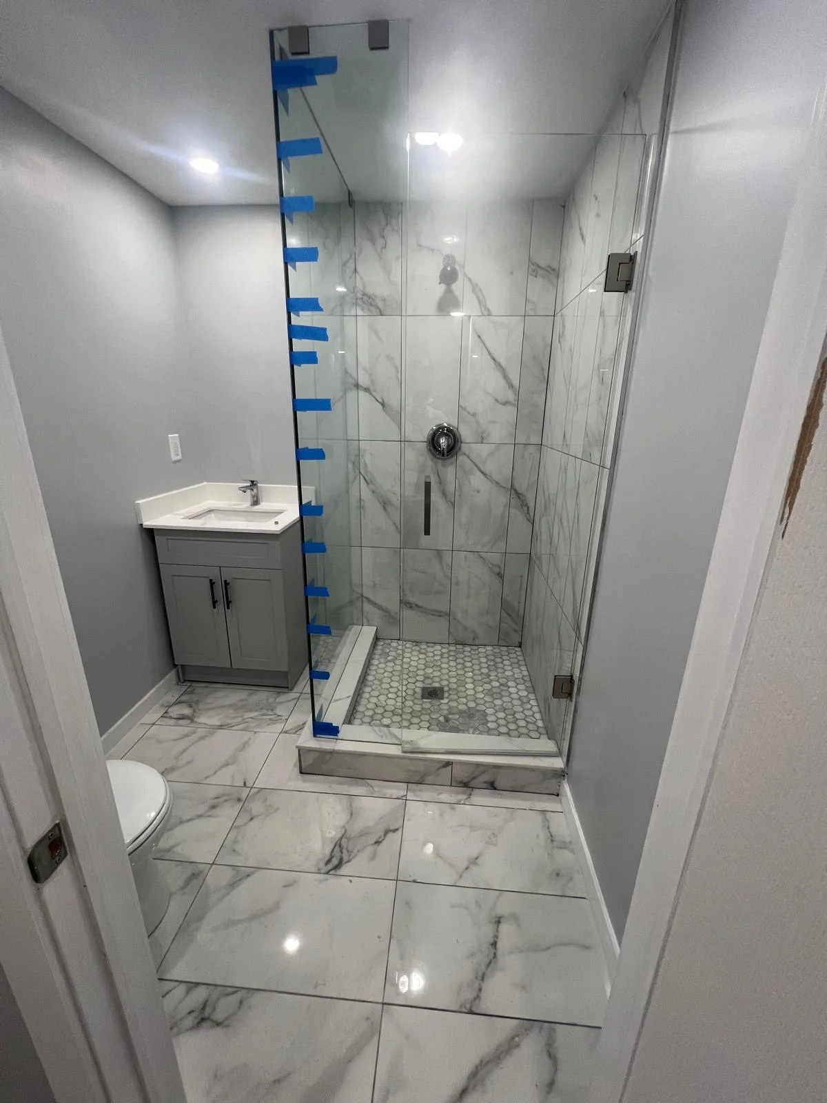 Basement bathroom with marble shower tile and vanity, glass being fitted