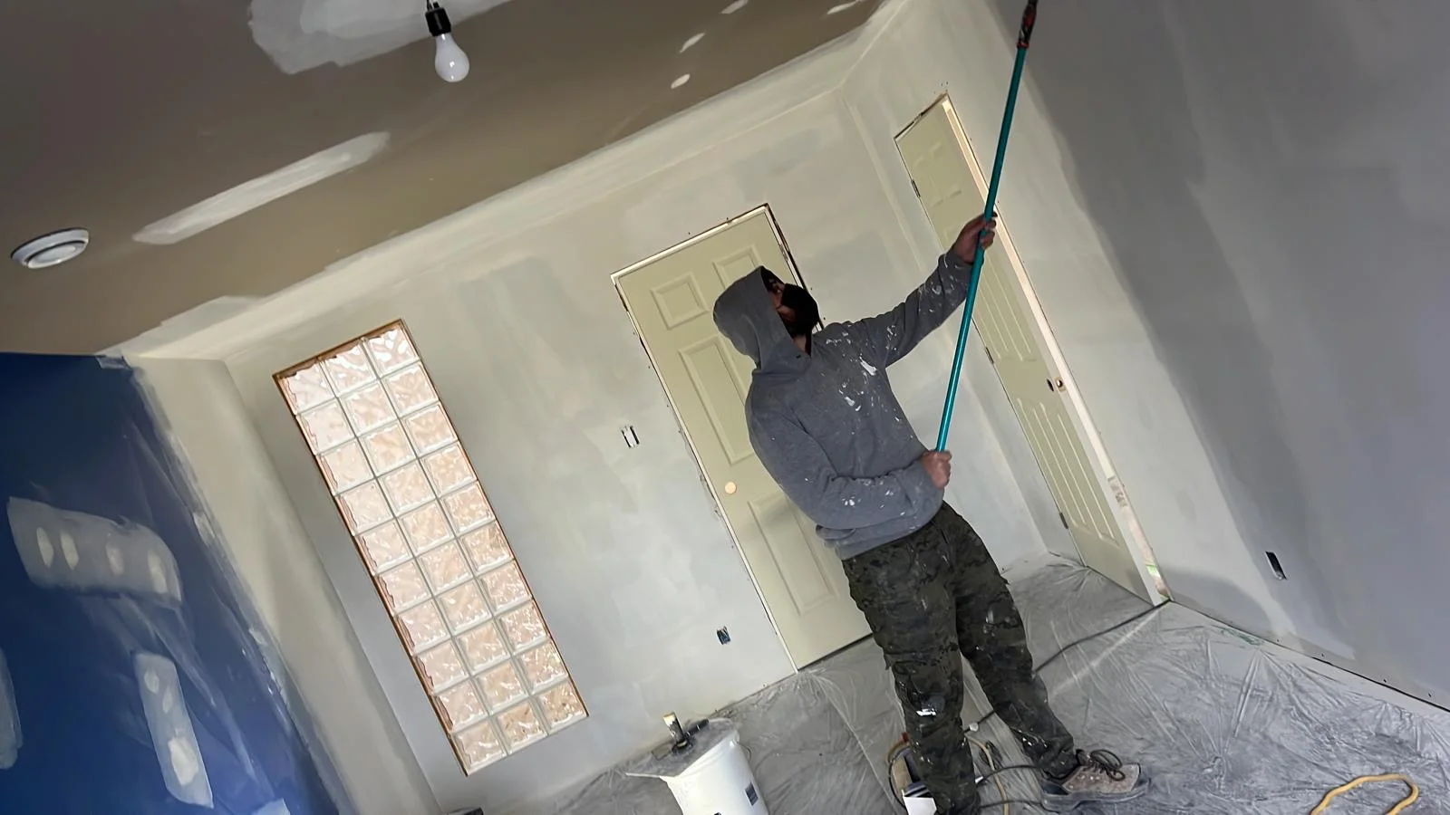 Contractor sanding a mudded ceiling seam with a pole sander